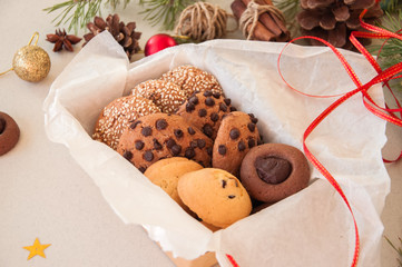 Christmas cookies gift box. Homemade festive baking concept, fir tree branches, balls, cinnamon, anise, red ribbon. Gray background.