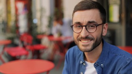 A closeup portrait of a handsome young man at the cafe - turning his head to the camera and smiling. Blurred background - Powered by Adobe