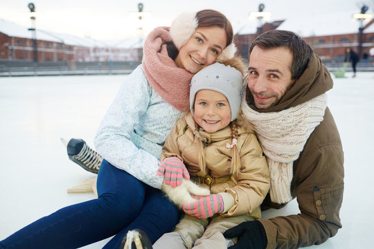 Affectionate and active family in winterwear sitting on skating rink