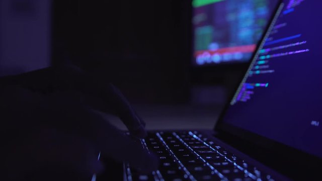Male hacker working on a computer in a dark office room.