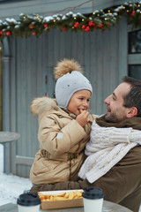 Affectionate father holding his daughter eating snack on festive event outdoors