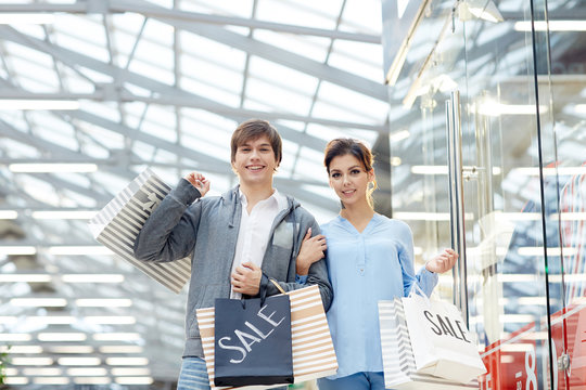 Affectionate man and woman with shopping bags looking at camera