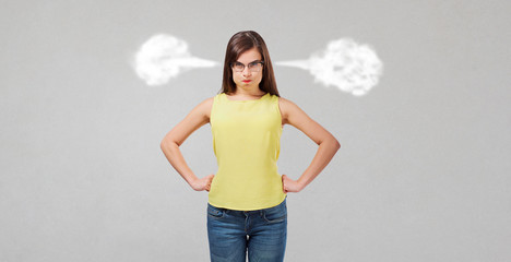 Dissatisfied wicked girl on a gray background. The woman lets out steam from ears. Human emotions.
