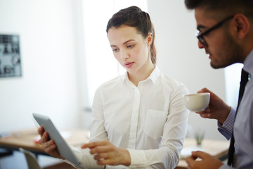 Confident businesswoman pointing at tablet display and explaining financial data to colleague