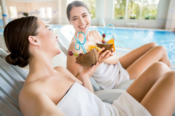Laughing girls with tropical cocktails enjoying rest at luxurious spa resort