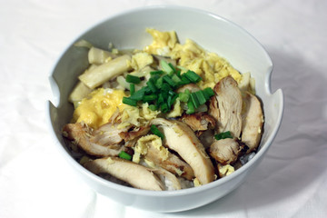 Baked chicken with eggs and mushrooms, topped with onion on the rice in the white bowl, on the white fabric. Fusion food of perfumed chicken and eggs with rice in the whiter container of food.