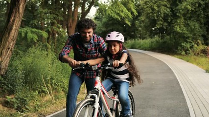 Closeup. Portrait of a little girl and her father. Dad teaching his daughter to ride a bike. He lets her go. Moving camera. Blurred background