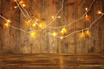 wood board table in front of Christmas warm gold garland lights on wooden rustic background. glitter overlay