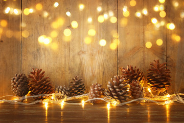Holiday image with Christmas golden garland lights and pine cones over wooden background