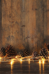 Holiday image with Christmas golden garland lights and pine cones over wooden background