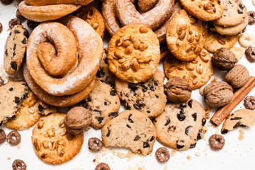 Culinary background of pastry shop, close up. Wholegrain cookies with peanuts and chocolate, baked roll with sugar powder on white table, top view. Delicious sweets and bakery, unhealthy food concept