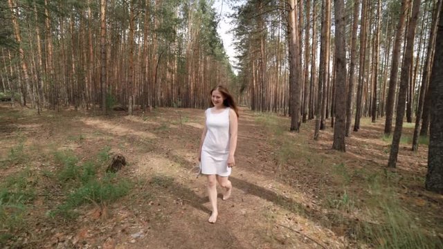 A girl in a white dress is walking in the woods