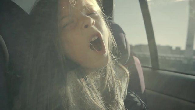 Pretty girl sits in a car and starts yawning. She looks relaxed and happy in slo-mo.