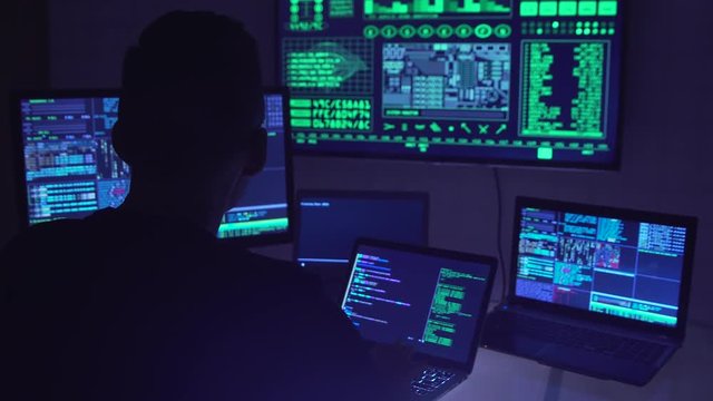 Male hacker working on a computer in a dark office room.