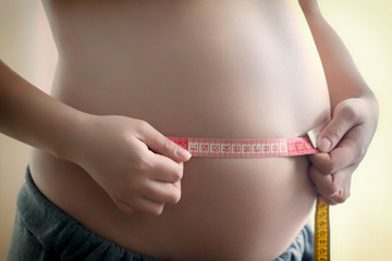 Pregnant girl measuring her stomach with a measuring tape, close up
