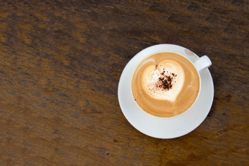 Top view of hot cappuccino coffee with heart shaped froth on classic wood table sprinkled coffee powder
