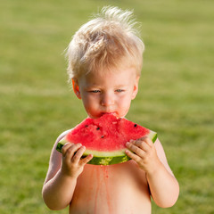 One year old baby boy eating watermelon in the garden