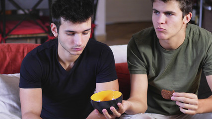Young male friends chilling on sofa with snacks spending time together and relaxing. 