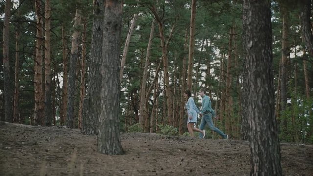 A young attractive couple runnig through the forest with their happy dog.Couple in love play with the dog shiba in pine forest .Couple kisses and hugs in summer forest.