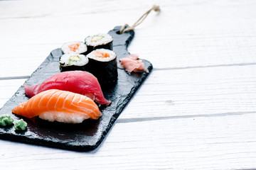 Sushi set served on a black slate. Sushi rolls and sashimi on a wooden white table. Seafood. Raw fish. White background. Wasabi. 