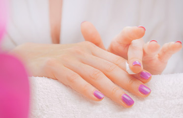 Application of cream on female hands with purple nail