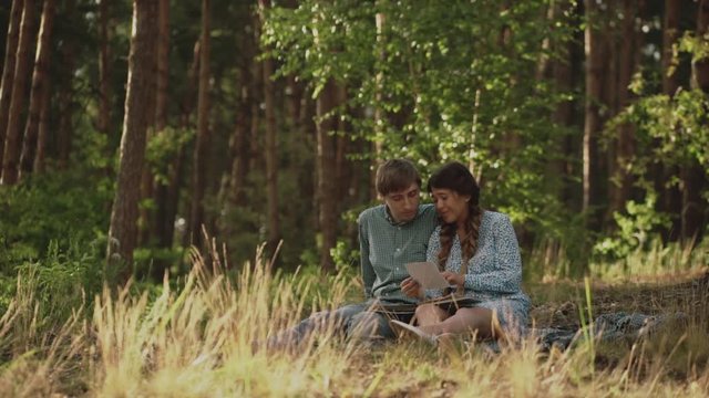 Couple sitting in picnic in the sunset forest. Family looking at their photo album sitting in the park. Happy couple with photo album.A young attractive couple walking through the forest with their
