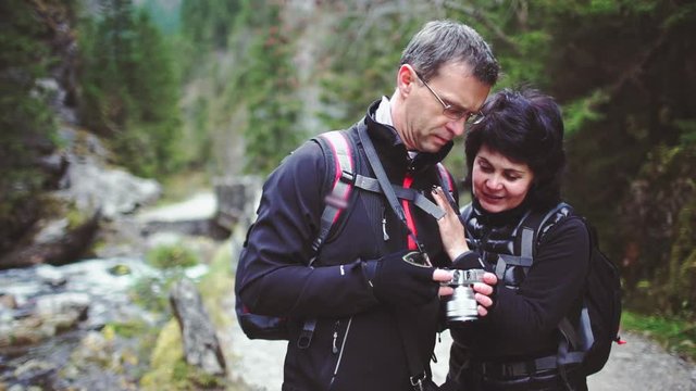 Adult Man and Woman Hikers Looking Through Photos They Took with Digital Camera. SLOW MOTION. Mature Tourists Couple enjoying mountain and forest nature. 