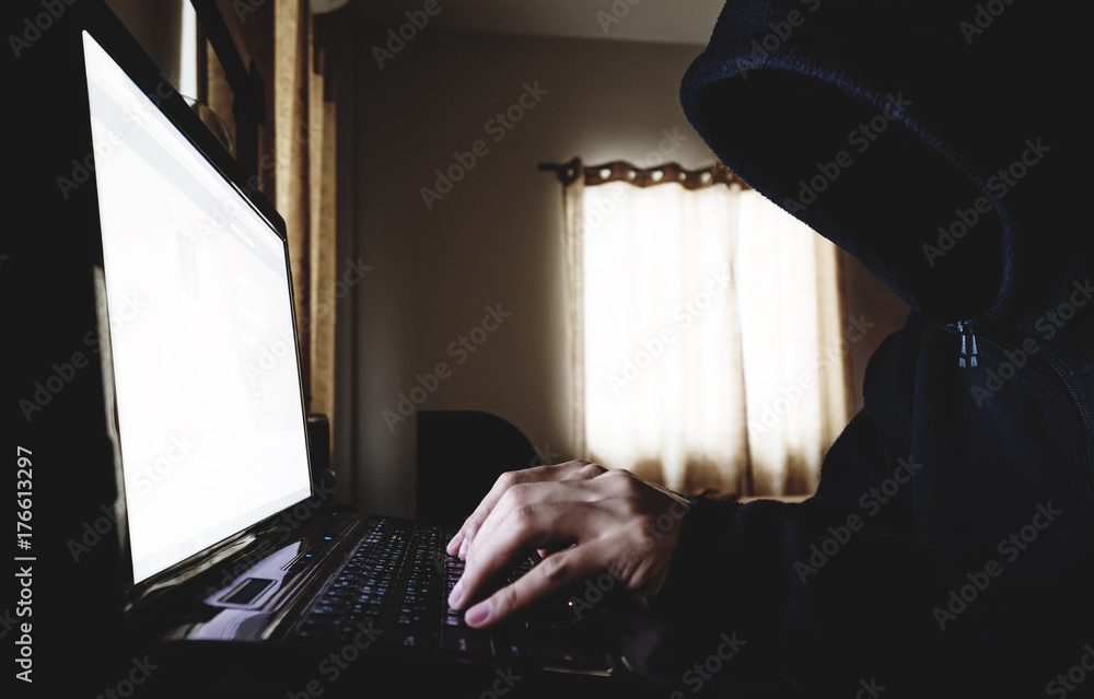Poster unidentified hacker in black hood using laptop computer in dark room. selective focus