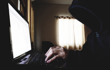 Unidentified Hacker in Black Hood using Laptop Computer in dark room. Selective focus