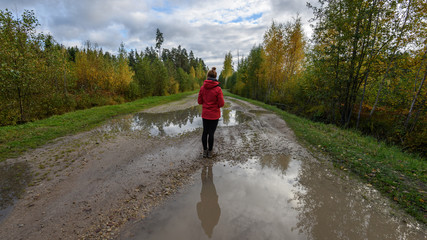 young woman in red jacket enjoying nature on dirt road. Latvia