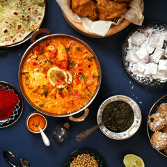 Indian cuisine on diwali holiday: tikka masala, samosa, patties and sweets with mint chutney and spices. Dark blue background. Square composition