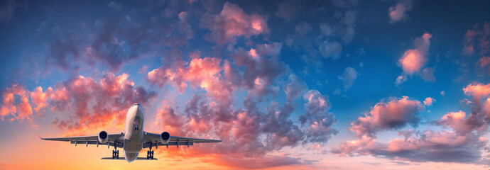 Naklejka premium Samolot i piękne niebo. Krajobraz z samolotem pasażerskim leci w błękitne niebo z chmurami czerwony, fioletowy i pomarańczowy o zachodzie słońca. Podróżować. Samolot pasażerski. Samolot komercyjny. Prywatny odrzutowiec