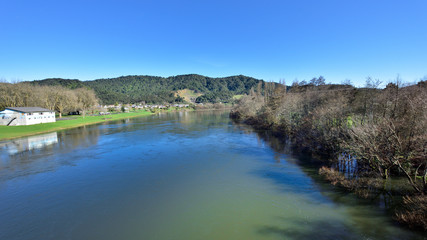 Fototapeta na wymiar River flowing alongside a village with low hills in the background