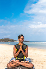 Asian yoga man practice yoga on the beach with a clear blue sky background. Yogi on the tropical beach of Bali island, Indonesia.