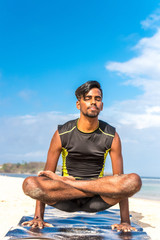 Asian yoga man practice yoga on the beach with a clear blue sky background. Yogi on the tropical beach of Bali island, Indonesia.