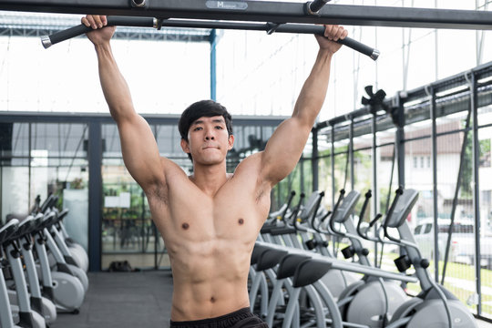 Young Man Execute Exercise With Machine In Fitness Center. Male Athlete Training In Gym. Sporty Guy Working Out In Health Club.