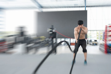 Fototapeta na wymiar young man execute exercise in fitness center. male athlete training with battle rope in gym. sporty guy working out in health club.