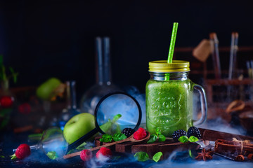 Smoothie jar with green helthy drink in a still life with berries, cinnamon, anise, magnifying...