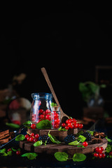 Jar with fresh currant and blackberry with wooden spoon on a black background. Laboratory and science concept. Magical still life with cinnamon and anise stars. Dark food photography.