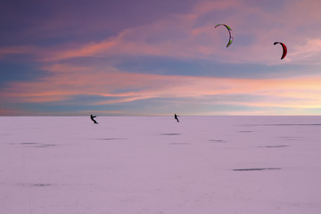 Kite surfers on frozen lake in the countryside from the Netherlands in winter at twilight