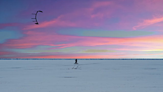 Kite surfer on frozen lake in the countryside from the Netherlands in winter at twilight