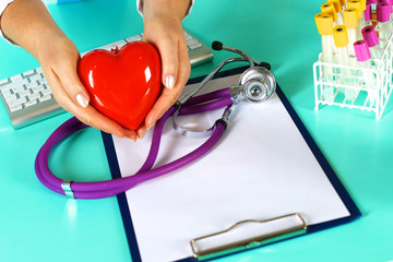 Female doctor with stethoscope holding heart. Doctor and patient sitting in the background
