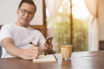 Fototapeta na wymiar closeup asian male hand is writing a note in a cafe,Choose a focal point at the hands of men