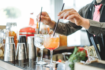 Bartender preparing different cocktails mixing with straws inside bar