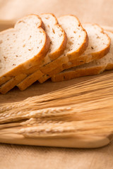 Wheat Bread Slices on a Cutting Board with Wheat. a side angle shot of slices of wheat bread angled on a cutting board with wheat in the foreground