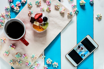 Top of view candy , fruit salad cake , coffee and phone on blue and white table