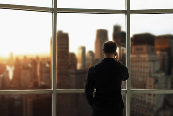 Man talking on the phone near a window with city views