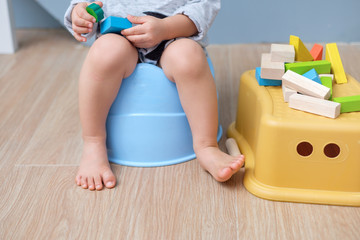 Closeup of legs of cute little Asian 18 months old toddler baby boy child sitting on potty playing with wooden blocks toy