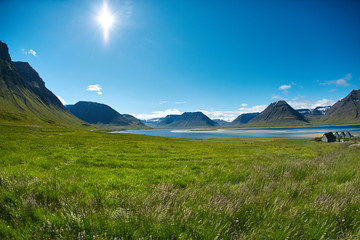 Fototapeta premium Travel to Iceland. beautiful sunrise over the ocean and fjord in Iceland. Icelandic landscape with mountains, blue sky and green grass on the foreground. View of Flateyri, a village in the north-west