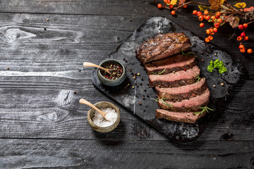 Sliced grilled roast beef with salt and pepper on marble plate on wooden old rustic table Black background. 